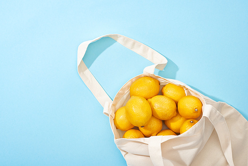 top view of ripe yellow lemons in cotton eco bag on blue background