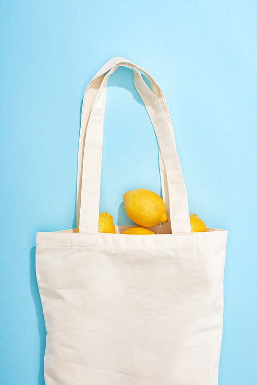 top view of ripe yellow lemons in cotton eco bag on blue background