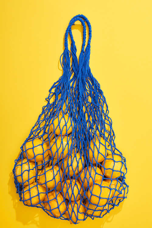 top view of ripe lemons in string bag on yellow background