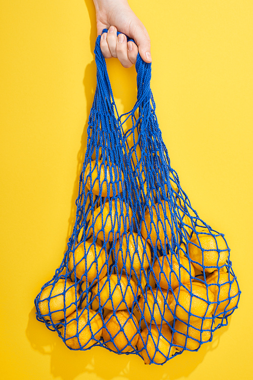 top view of ripe lemons in string bag on yellow background