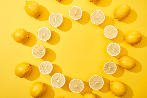 top view of ripe cut and whole lemons arranged in round frame on yellow background with copy space