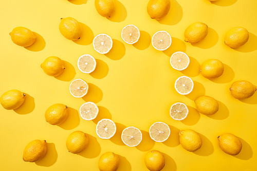 top view of ripe cut and whole lemons arranged in round frame on yellow background with copy space