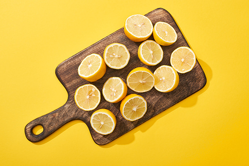 top view of ripe cut lemons on wooden cutting board on yellow background