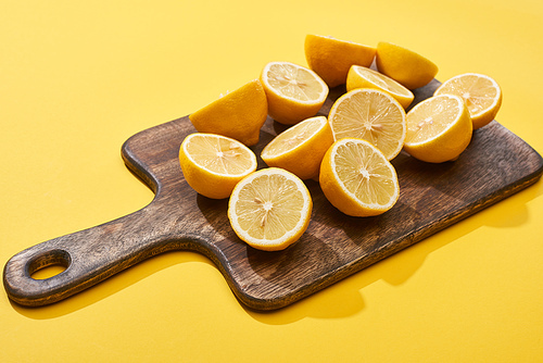 ripe cut lemons on wooden cutting board on yellow background