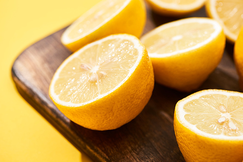 close up view of ripe cut lemons on wooden cutting board on yellow background