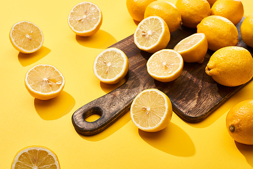 ripe cut and whole lemons on wooden cutting board on yellow background
