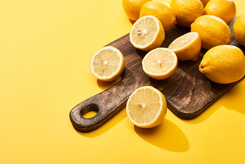 ripe cut and whole lemons on wooden cutting board on yellow background with copy space