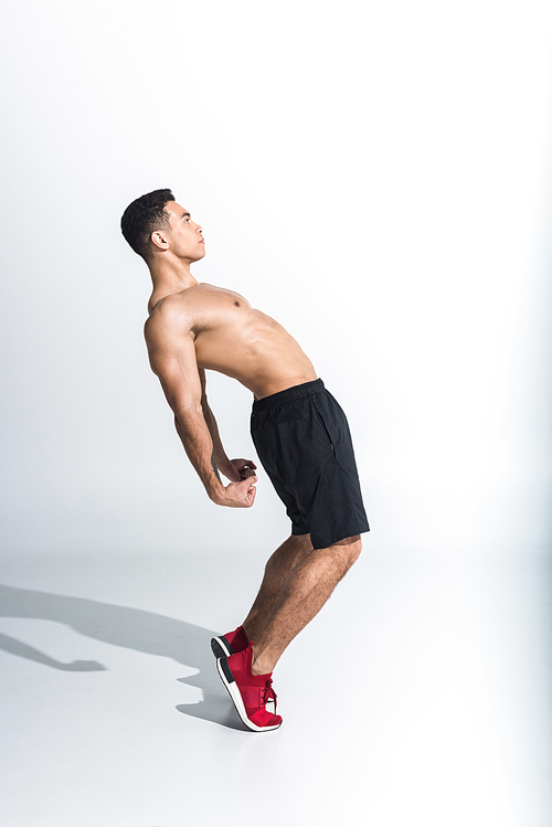 side view of sportive, handsome mixed race man in black shorts and red sneakers warming up on white