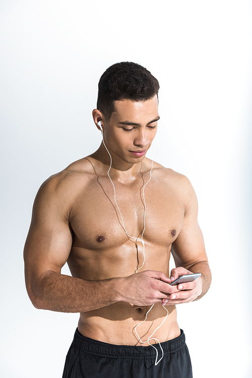 handsome sportive mixed race man in earphones holding smartphone and listening music on white