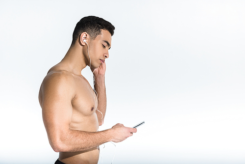 side view of handsome sportive mixed race man listening music in earphones on white