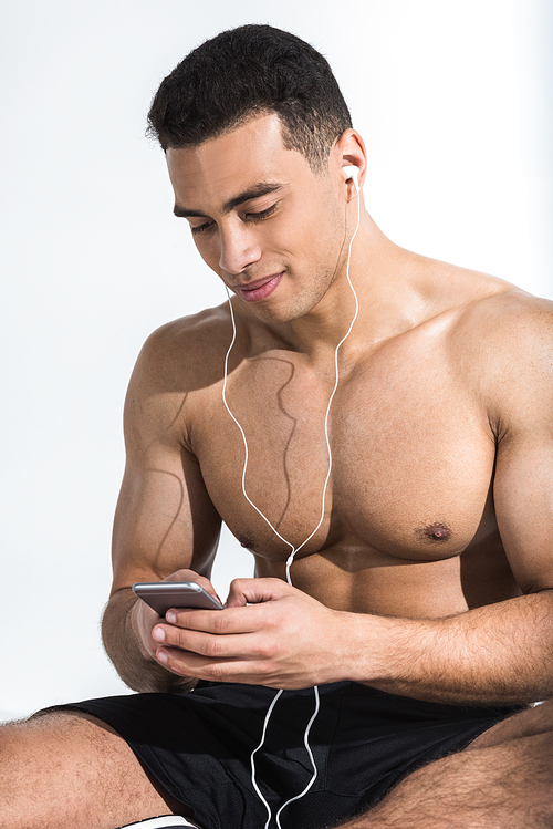 handsome athletic man with smartphone listening music and smiling on white