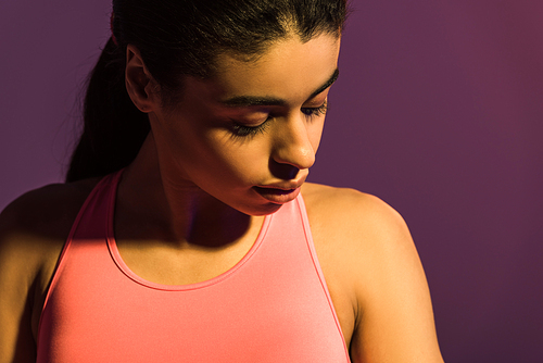 beautiful african american girl in pink sports bra looking down  isolated on purple
