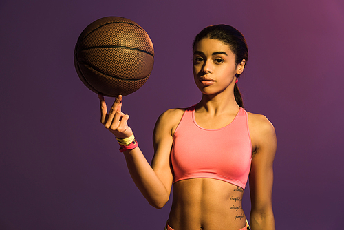 pretty african american girl in pink sports bra holding brown ball and  on purple background