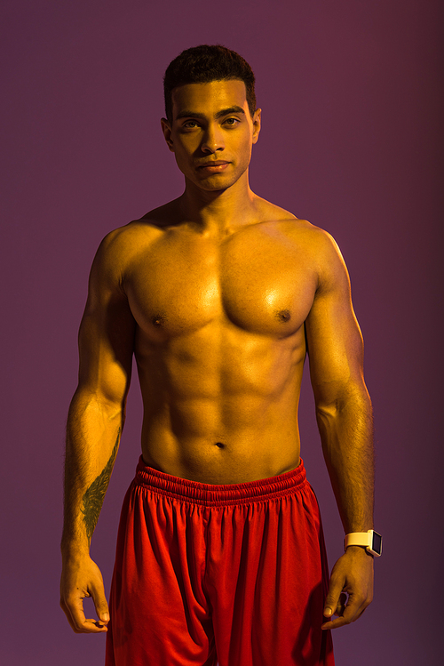 handsome sportive mixed race man in smart watch and red shorts  on purple background