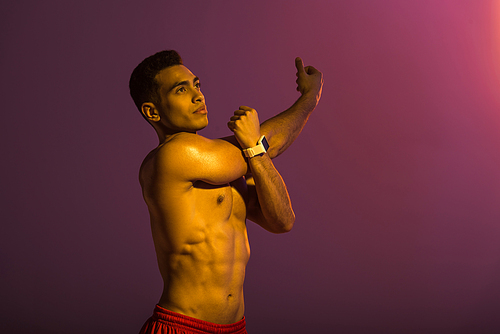handsome sportive man in smart watch stretching on purple background