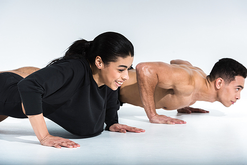 smiling african american girl and mixed race man doing push ups on white
