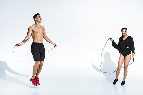 smiling african american girl and handsome mixed race man training with jump ropes on white background