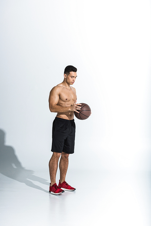 handsome shirtless mixed race man in black shorts and red sneakers holding ball on white