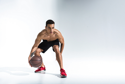 athletic mixed race man in red sneakers playing ball on white background