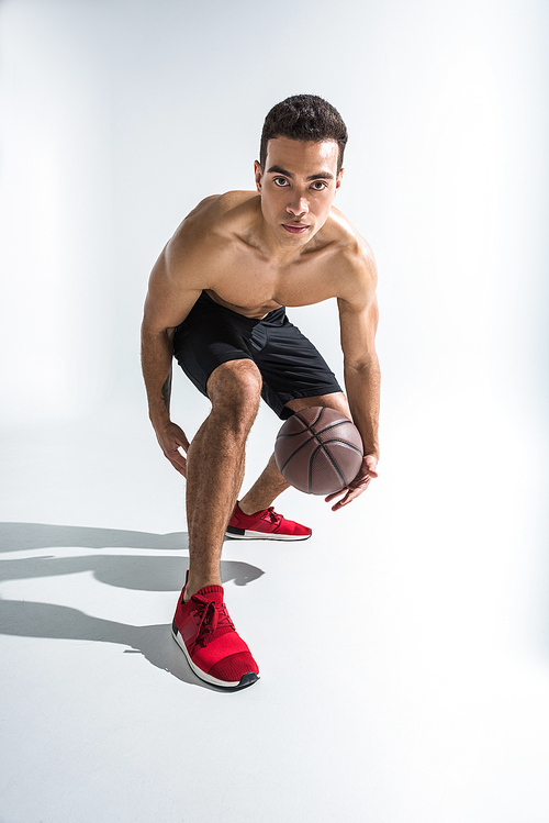 good-looking sportive mixed race man in red sneakers playing ball on white