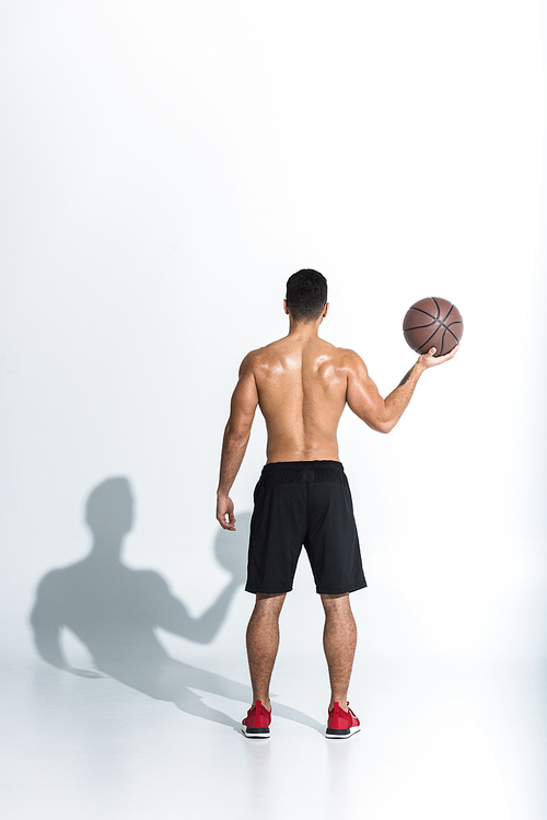 back view of athletic man in black shorts holding brown ball on white background