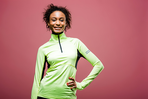 beautiful african american sportswoman in track jacket  and smiling isolated on pink