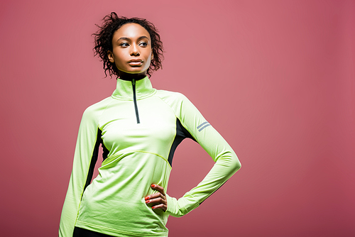 beautiful african american sportswoman in track jacket posing with hand on hip isolated on pink with copy space