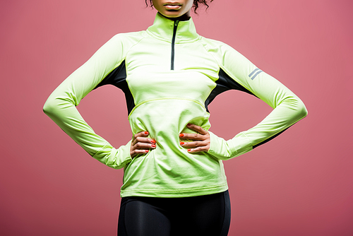 cropped view of african american sportswoman in track jacket posing with hands akimbo isolated on pink