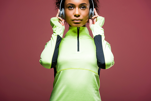 beautiful african american sportswoman in headphones and track jacket isolated on brown