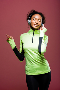 beautiful african american sportswoman in headphones listening music with eyes closed isolated on brown