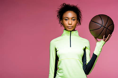 beautiful african american sportswoman  and holding basketball isolated on pink with copy space
