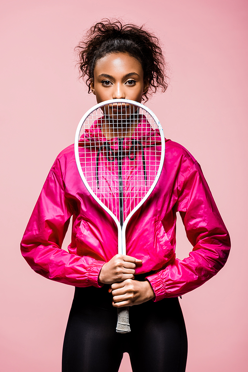 beautiful african american sportswoman posing with tennis racket isolated on pink