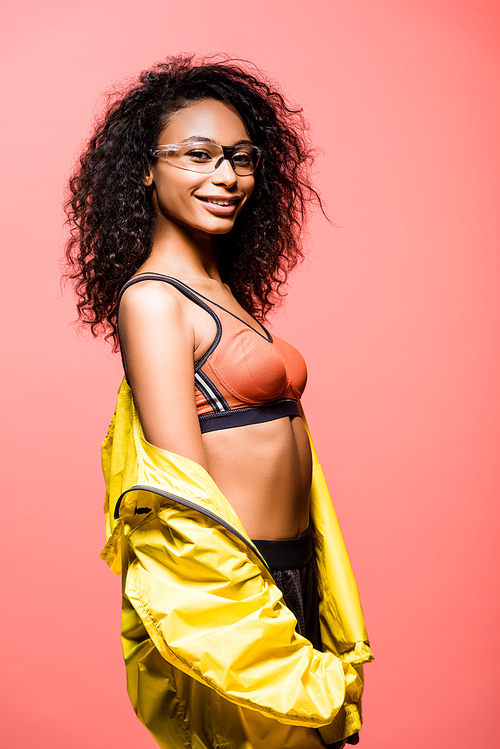 beautiful smiling african american sportswoman in glasses posing and  isolated on coral