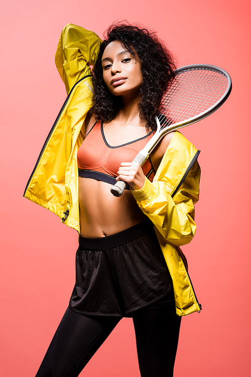 beautiful african american sportswoman  and holding tennis racket isolated on coral