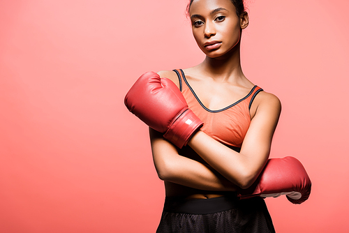 confident african american sportswoman in boxing gloves posing isolated on coral with copy space