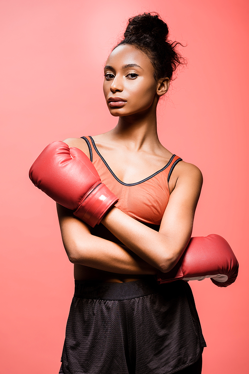 beautiful african american sportswoman in boxing gloves  isolated on coral