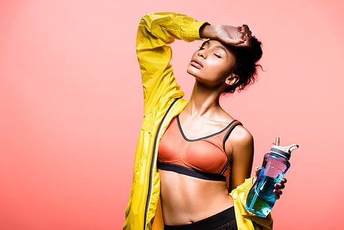 beautiful african american sportswoman with sport bottle posing isolated on coral with copy space