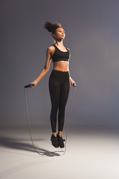 athletic african american sportswoman exercising with skipping rope on grey