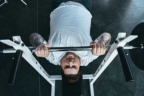 top view of Overweight tattooed man in white t-shirt training with barbell at gym