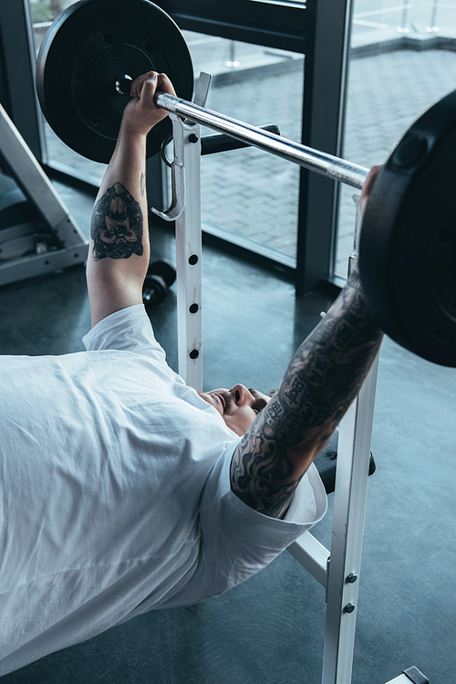 Overweight tattooed man training with barbell at gym
