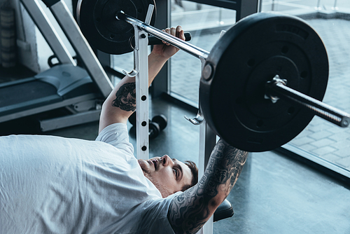Overweight tattooed man training with barbell at gym
