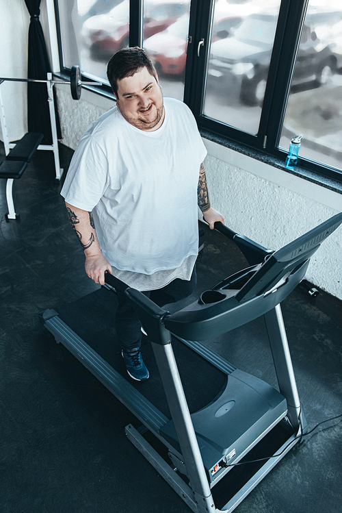 smiling overweight tattooed man  while running on treadmill at sports center