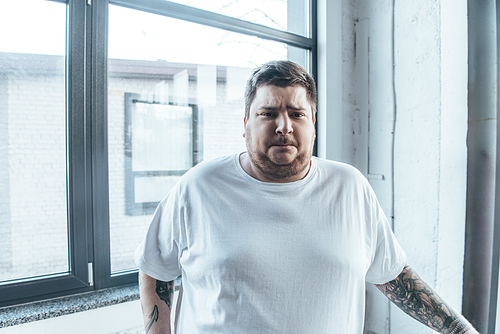 overweight tattooed man in white t-shirt  at gym