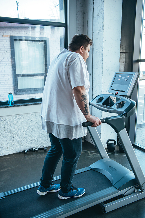 overweight tattooed man running on treadmill at sports center
