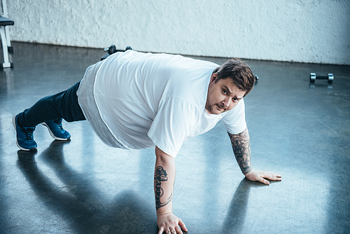 overweight tattooed man  while doing push up exercise at sports center