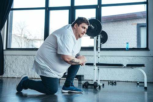 overweight tattooed man in white t-shirt stretching at sports center