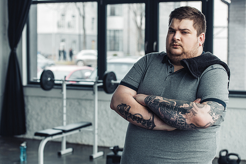 overweight tattooed man with towel and crossed arms  at gym