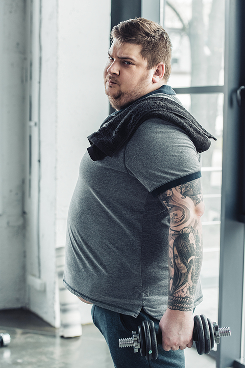 Obese tattooed man  while exercising with dumbbell at sports center