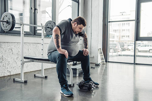 tired Overweight man sitting on bench after exercising with dumbbells at gym