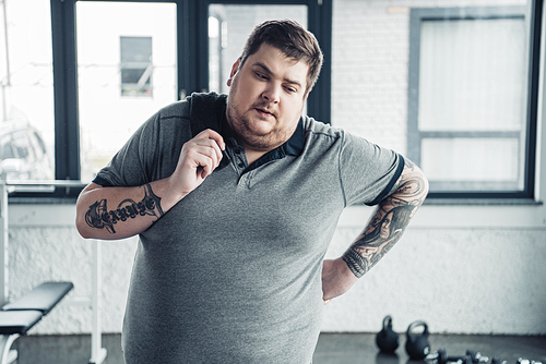 overweight tattooed man holding towel at sports center